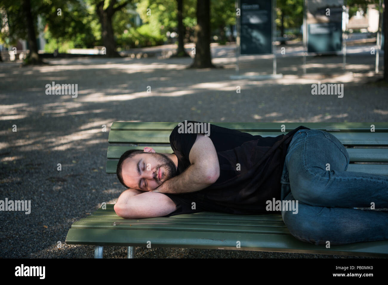 Young man lying down sleep on bench in the park and wakes up after rest