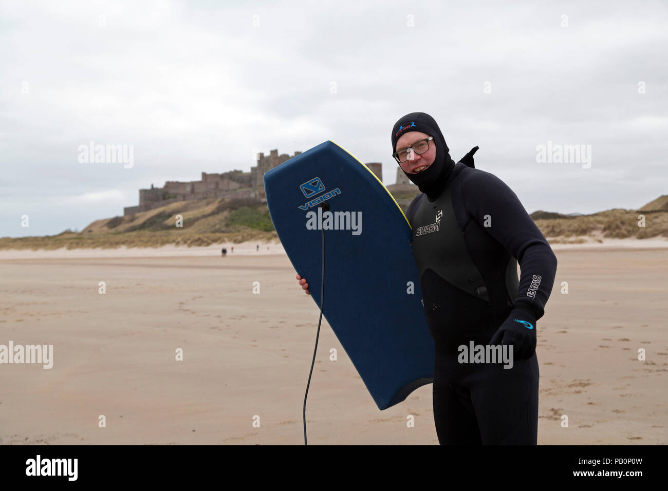 Man holding a bodyboard on Bamburgh Beach in Northumberland, England. He is participating the the Northern Bootcamp, a residential boot camp. Stock Photo