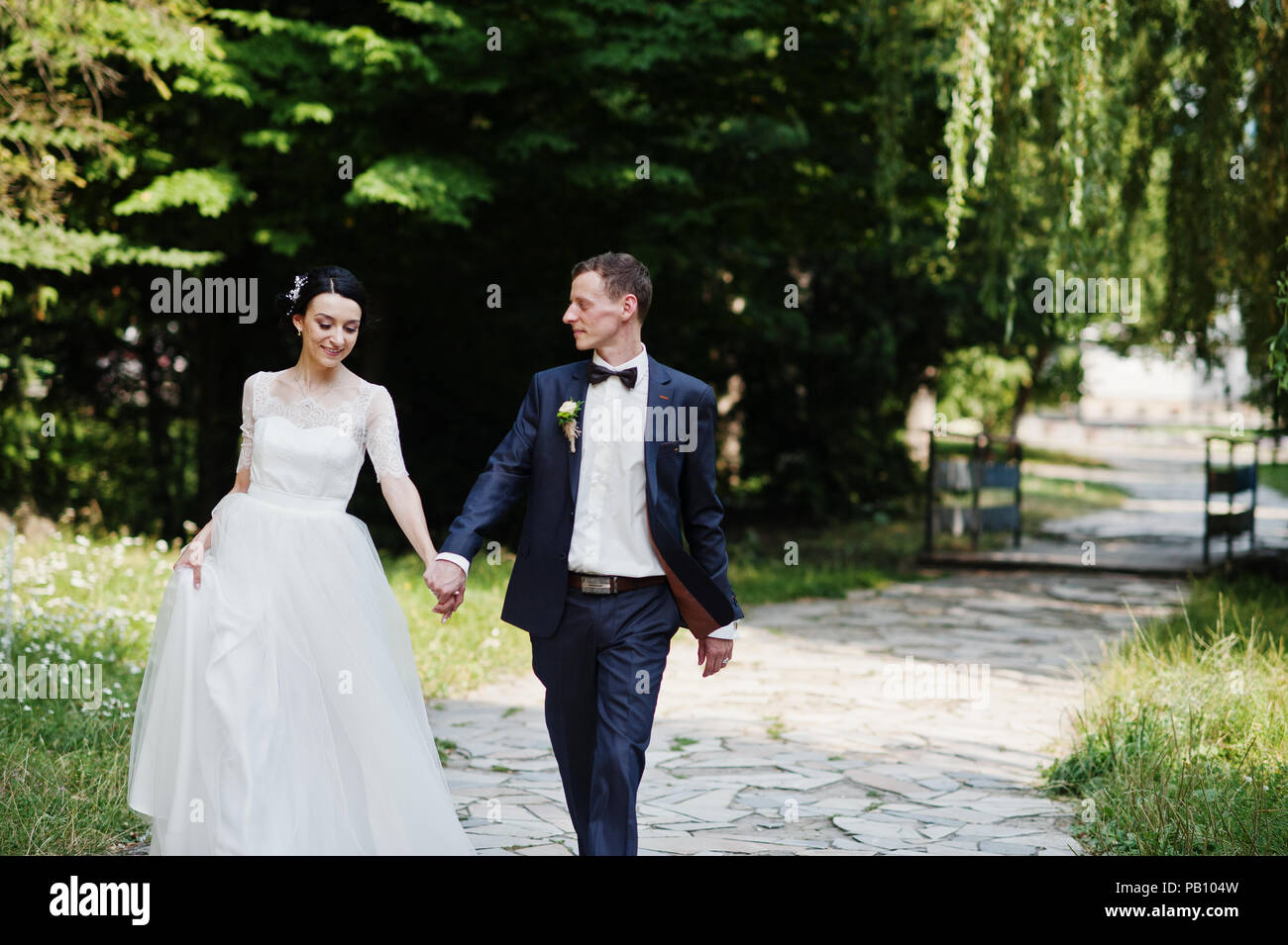 Gorgeous wedding couple holding hands and walking in the park on the ...
