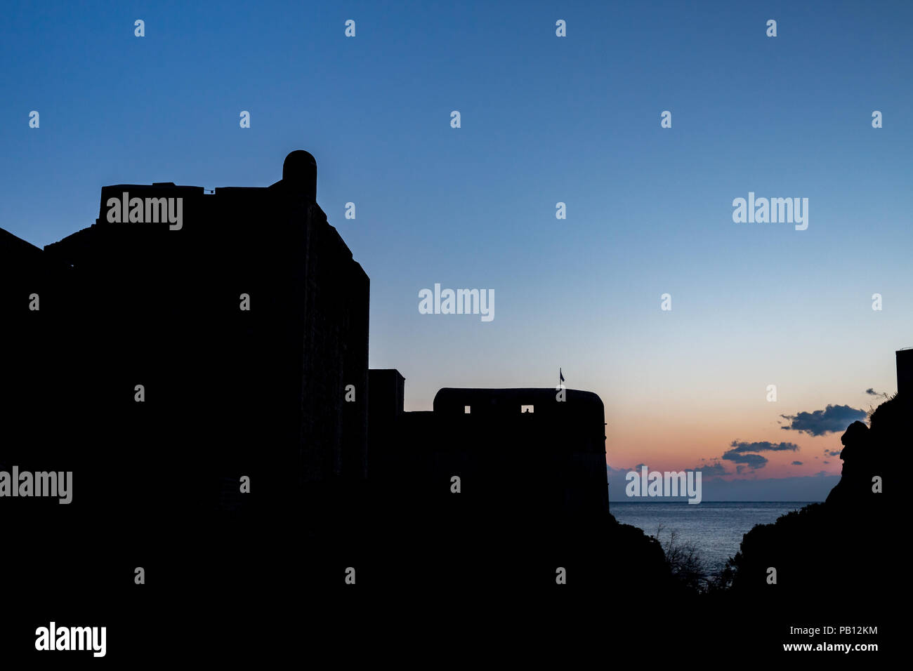The black silhouette of the Dubrovnik castle tower on sunset with the colorful sky and the dark blue Adriatic Sea, almost clear sky with few small clo Stock Photo