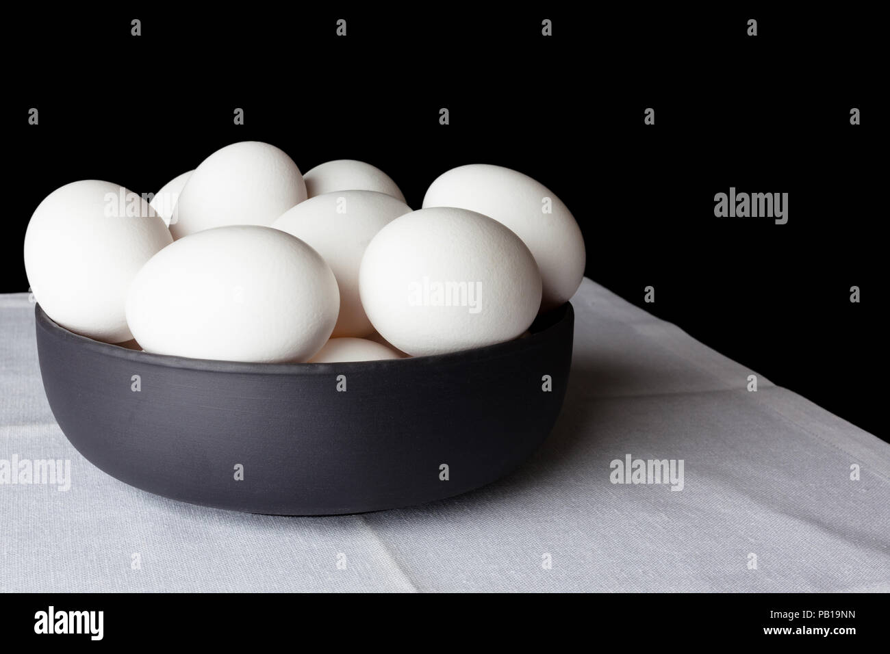 White eggs in a black bowl on white linen napkin on black background from side off centre composition Stock Photo