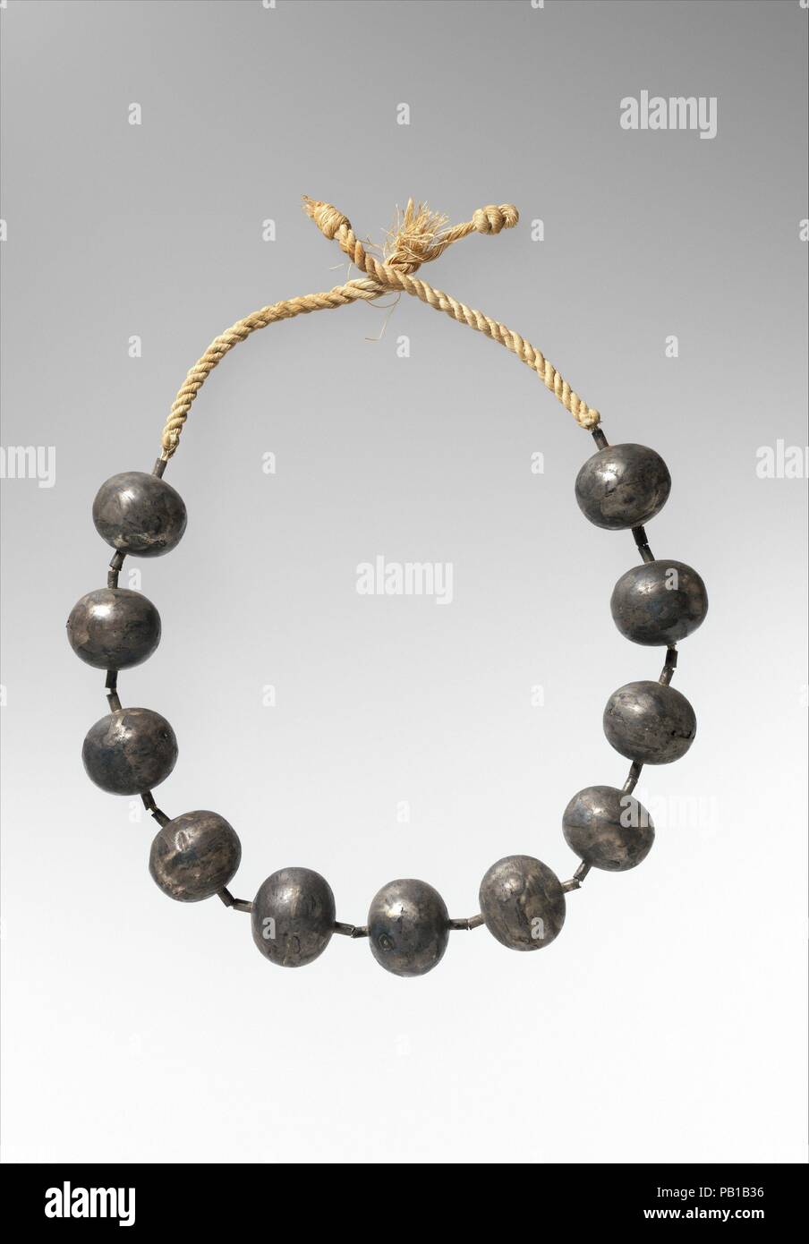 Necklace of Wah. Dimensions: L. of necklace  70.5 cm (27 3/4 in.); Greatest diam. 3.2 cm (1 1/4 in.); Smallest diam. 2.5 cm (1 in.). Dynasty: Dynasty 12. Reign: reign of Amenemhat I, early. Date: ca. 1981-1975 B.C..  After Wah's mummy had been partially wrapped, this necklace of silver beads was tied around the neck.  The beads were strung on twelve or more strands of thread that were then twisted through ties of thick linen cord.  Three other necklaces had been placed on the mummy in the same position.  One of these is made of gold beads (40.3.17); one is made of blue faience beads (40.3.18); Stock Photo