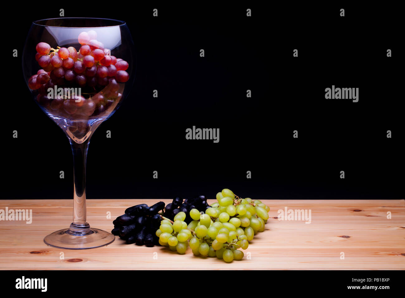 Glass of red win grapes. Grape variety still life. Classic painterly image. Red green and black grape varieties. Summer fruit on farmhouse kitchen tab Stock Photo