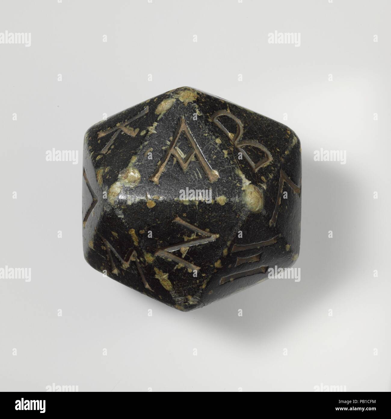 Greenstone polyhedron inscribed with letters of the Greek alphabet. Culture: Greek. Dimensions: Width (point to point greatest width): 3 3/8 in., 22.9oz. (8.6 cm, 647.9g)  Width (point to point smallest): 3 5/16 in. (8.4 cm)  Width (Side to side): 2 13/16 in. (7.2 cm). Date: 2nd-1st century B.C..  The polyhedron has 20 sides, each inscribed with a letter of the Greek alphabet from A (alpha) to Y (upsilon), so that only the last three letters (chi, psi, and omega) are missing. See a faience example (37.11.3) also displayed in this case. Museum: Metropolitan Museum of Art, New York, USA. Stock Photo