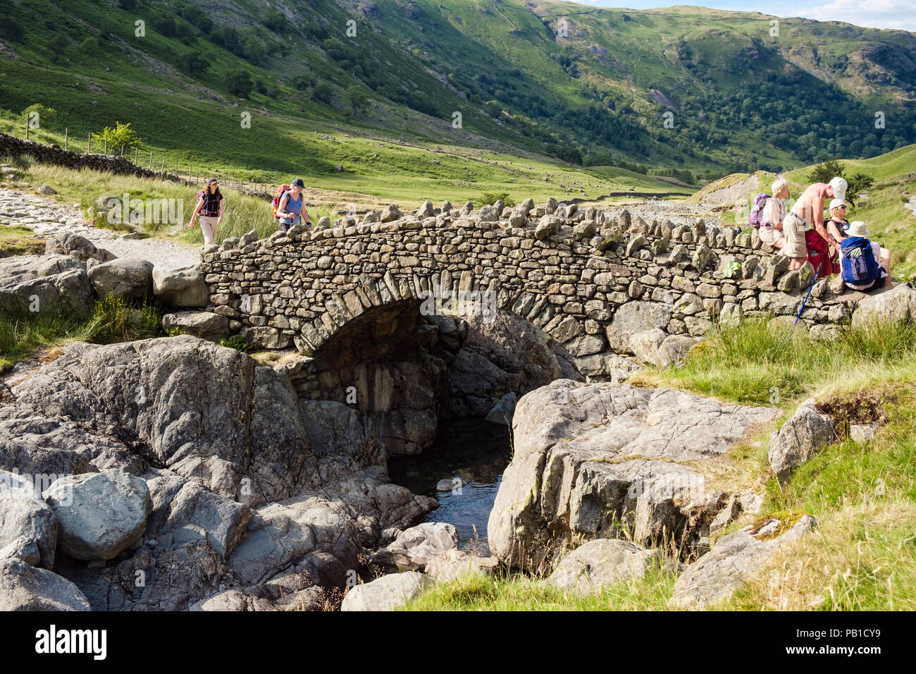 Hikers hiking on track over Stockley Bridge in Lake District National Park in summer. Seathwaite, Cumbria, England, UK, Britain Stock Photo