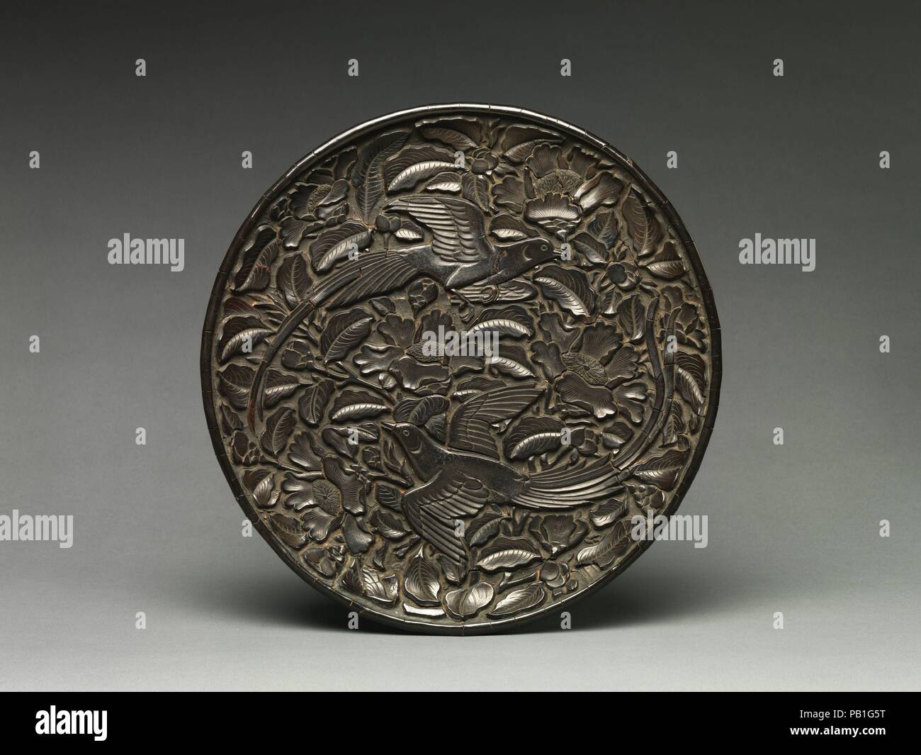 Round dish with long-tailed birds and flowers. Culture: China. Dimensions: H. 1 7/16 in. (3.7 cm); Diam. 12 3/8 in. (31.4 cm). Date: second half of the 14th century.  A sophisticated example of the two-bird design, the compact composition of this dish features flowers and long-tailed birds (shoudai, or paradise flycatchers)--a symbol of a rewarding career and long life--carved in a three-dimensional effect. Museum: Metropolitan Museum of Art, New York, USA. Stock Photo