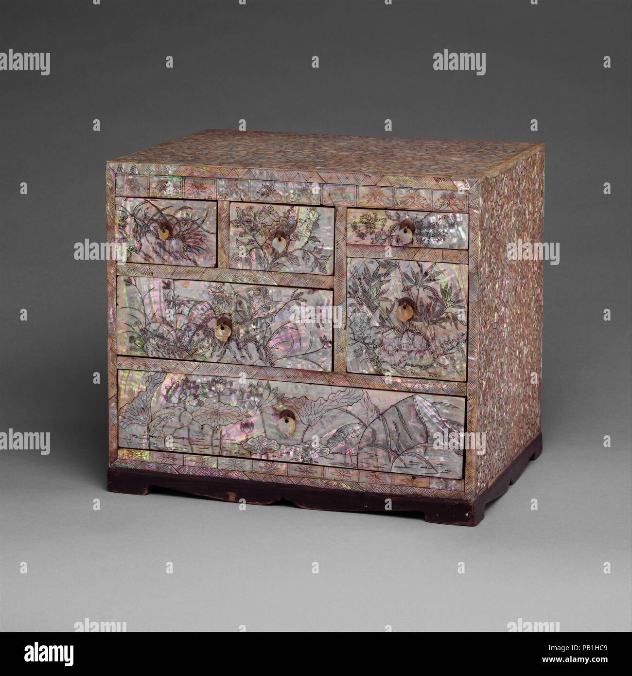Small Chest of Drawers with Decoration of Flowers, Birds, and Insects. Culture: Korea. Dimensions: H. 11 3/8 in. (28.9 cm); W. 12 7/8 in. (32.7 cm); D. 9 7/8 in. (25.1 cm). Date: early 20th century.  This chest is an excellent example of an early twentieth-century lacquer box with allover mother-of-pearl decoration. The incised floral motifs filled with black ink or charcoal make the piece particularly striking. The shape, size, and compartments suggest that this chest held writing or cosmetic paraphernalia. Museum: Metropolitan Museum of Art, New York, USA. Stock Photo