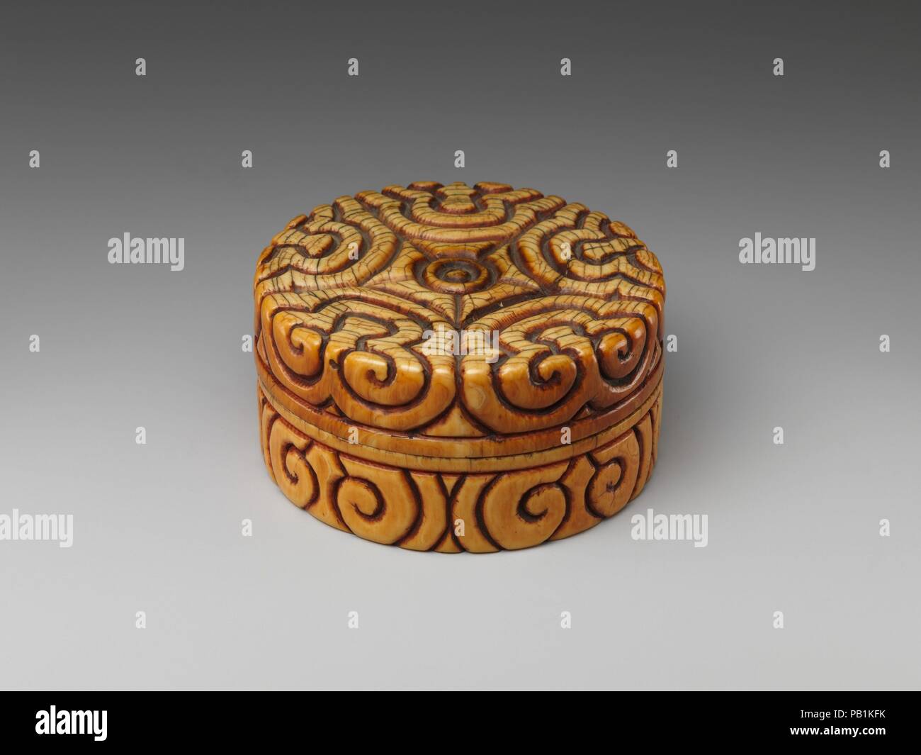 Box with pommel-scroll design. Culture: China. Dimensions: H. 1 7/8 in. (4.8 cm); Diam. 3 1/2 in. (8.9 cm). Date: late 13th-14th century.  The decoration covering the surface of this box is sometimes known as a pommel-scroll design because it resembles the shape of sword's pommel. A flowering plum tree and crescent moon made of ivory, gold leaf, lacquer, and glass, are inlaid into the interior of the cover. The motif may allude to any number of earlier poems that evoke the shadows of plum blossoms by moonlight in a night filled with their scent. Museum: Metropolitan Museum of Art, New York, US Stock Photo