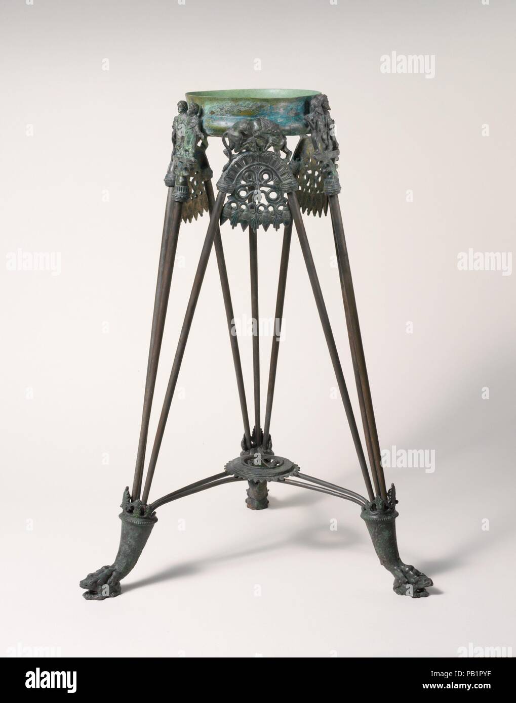 Bronze tripod. Culture: Etruscan. Dimensions: H. as restored 26 in. (66.1 cm). Date: ca. 525-500 B.C..  The city of Vulci was famous in antiquity for its production of luxury bronzes. One popular type of item was the tripod, an elaborate stand to support either a cauldron or a brazier. Tripods were produced at Vulci for about seventy years, from about 540 to 470 B.C. This example is elaborately decorated with lion's-paw feet surmounting frogs, wild beasts attacking their prey on the arches above elegant palmette motifs, and a pair of mythical subjects at the top of each of the vertical rods. T Stock Photo