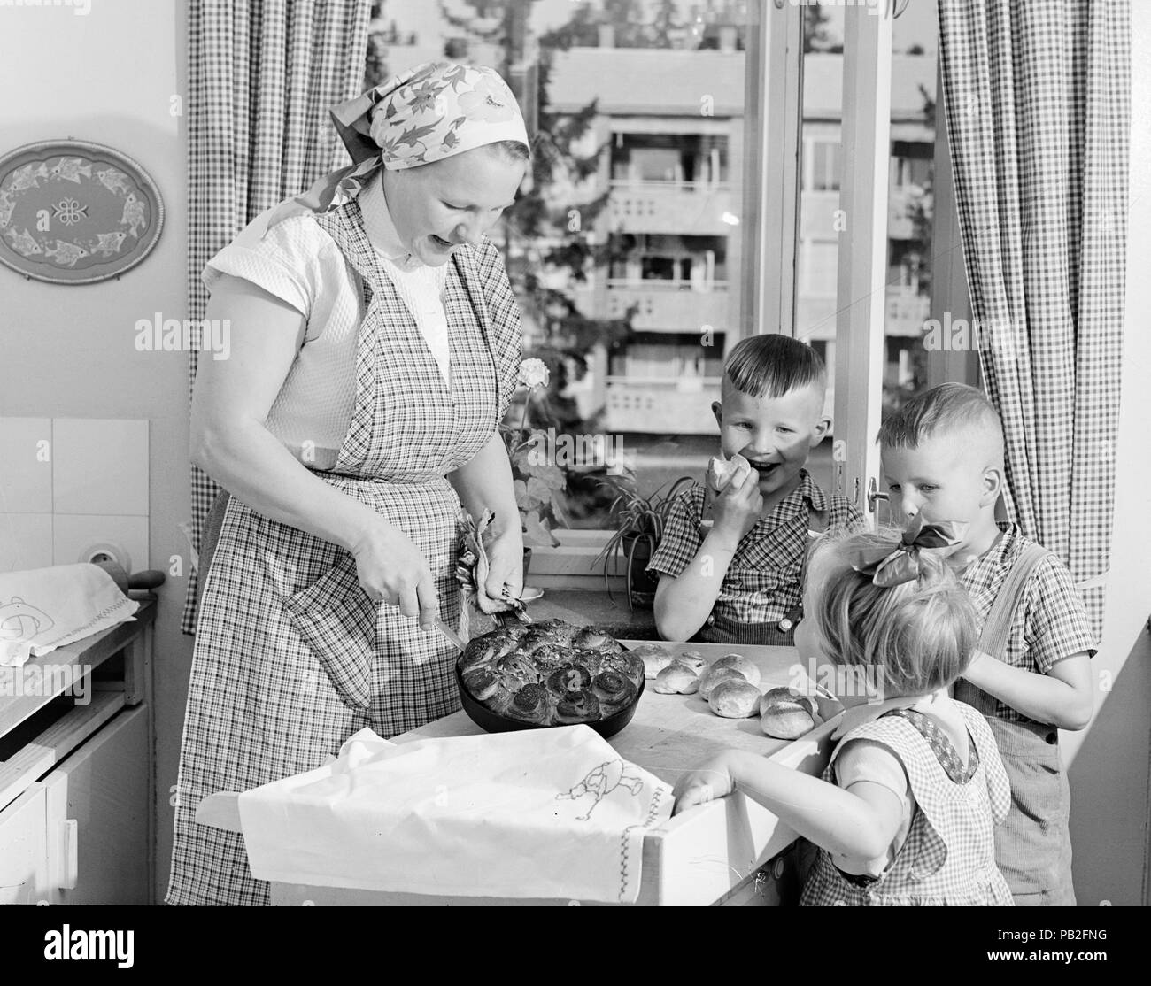 Mother baking buns for her children in 1950s apartment Finland Stock Photo