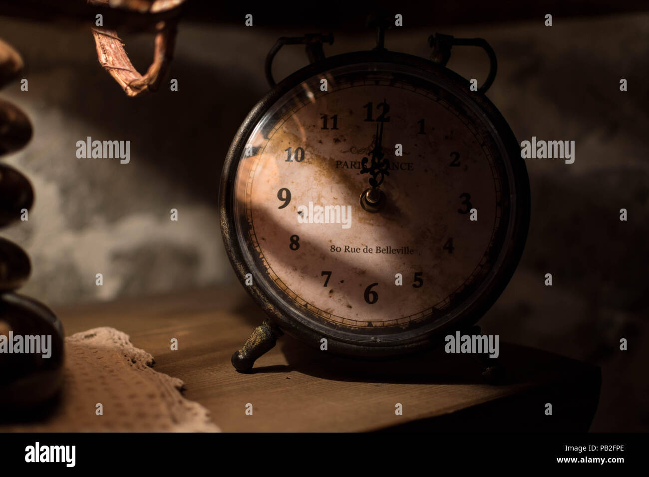 An old clock on a night stand lit partly by a night lamp with thatched hood, creating a calm an romantic mood. An address in Paris, Europe, is on the  Stock Photo