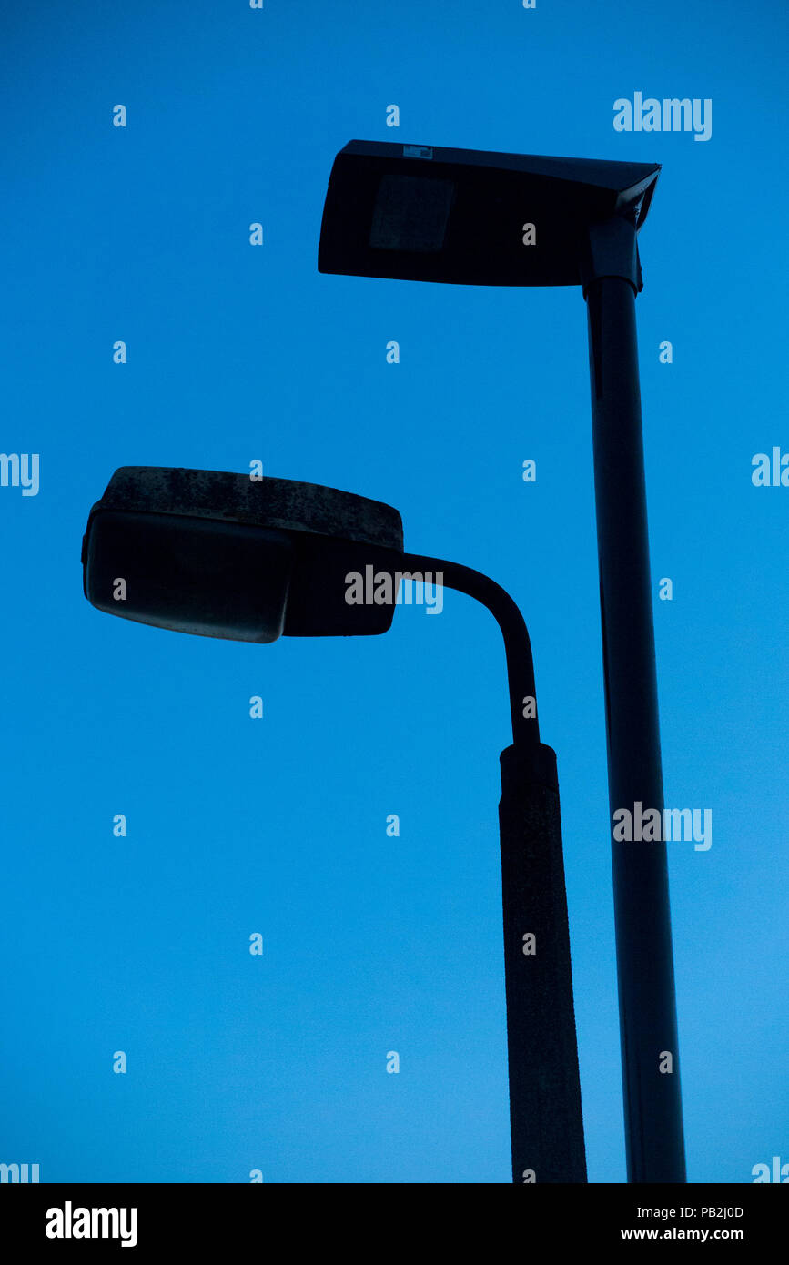 Silhouette of street lamp head / light / lights / lamps of an older sodium technology (left) which are in the process of being replaced by LEDs / LED (right). (100) Stock Photo
