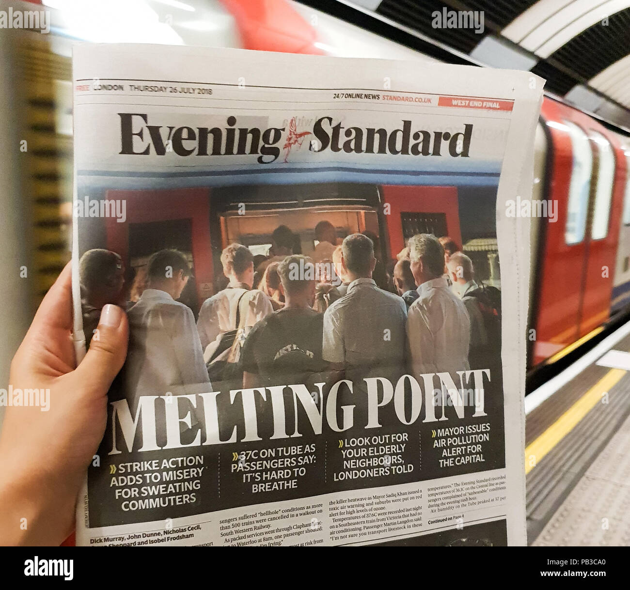 Underground platform. London. UK 26 July 2018 - A person holds the latest edition of London Evening Standard with the headline “Melting Point” on the hottest day of the year as a train approaches the station platform. Heathrow Airport saw the day's highest temperature of 35 degrees celsius. Temperature reached over 35 degrees celsius on the underground trains and commuters have complained of unbearable travel conditions.  Credit: Dinendra Haria/Alamy Live News Stock Photo