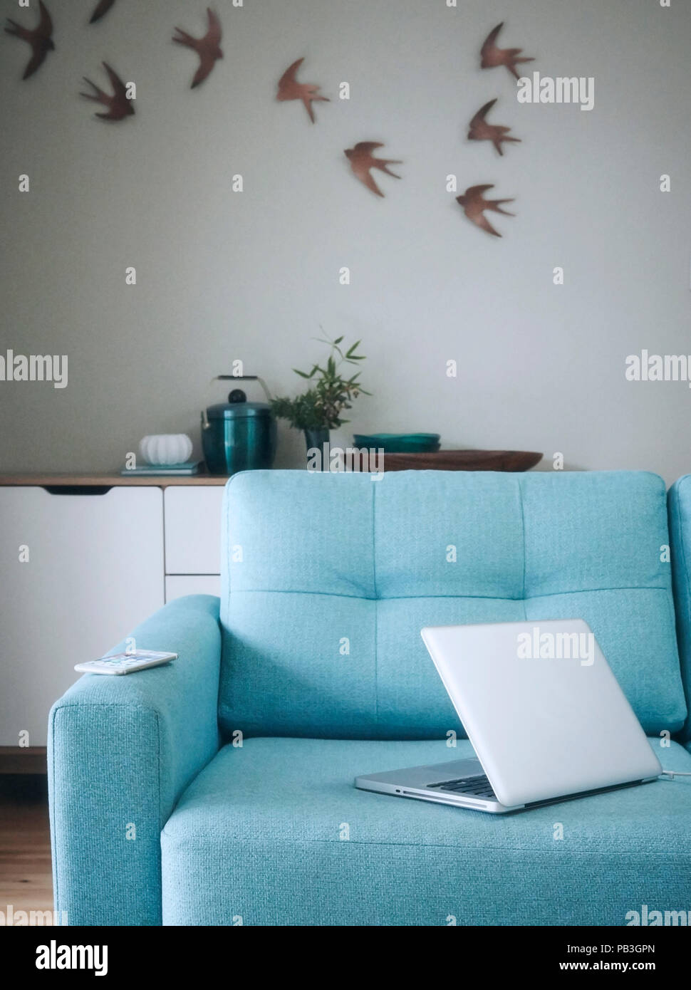 Laptop weathered to a smartphone on a teal sofa in a light airy living room. Stock Photo