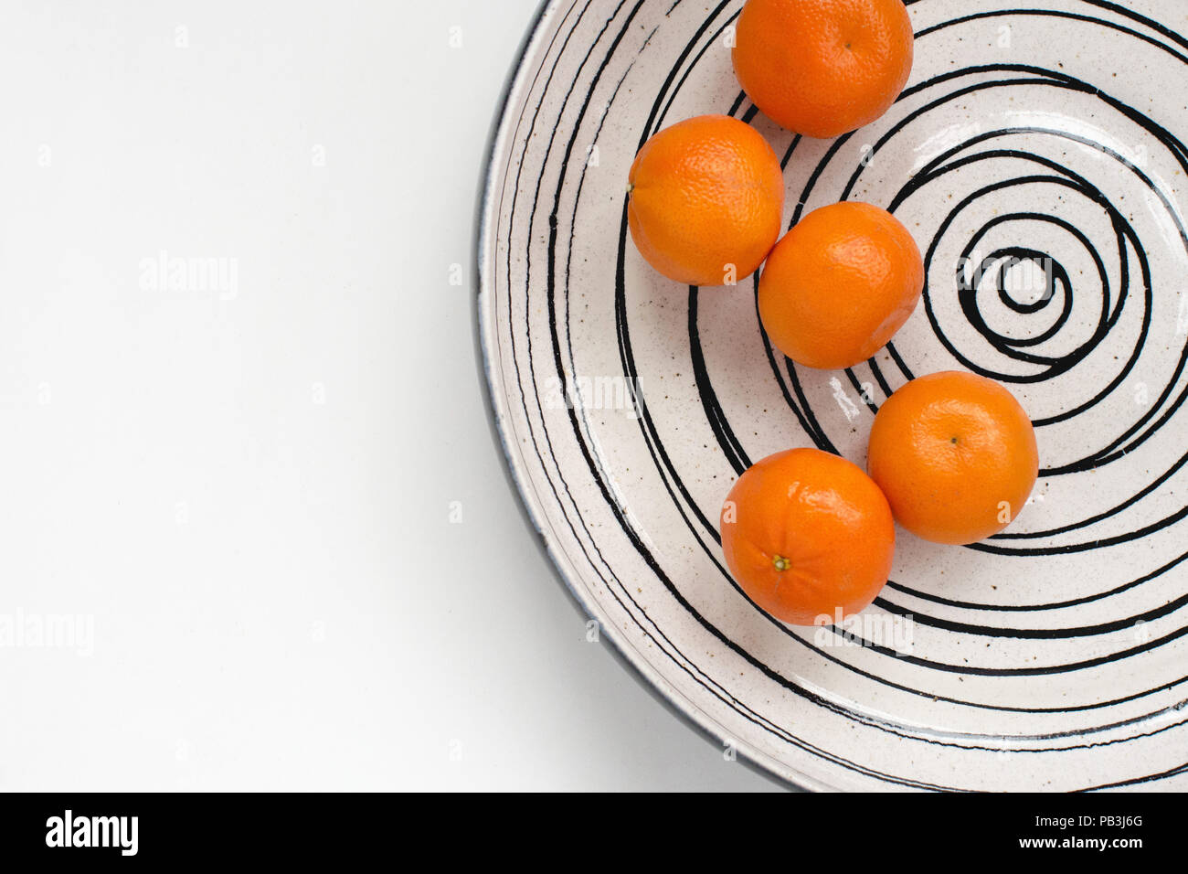Five easy peel tangerines in a large fruit bowl with a spiral pattern on a white background Stock Photo