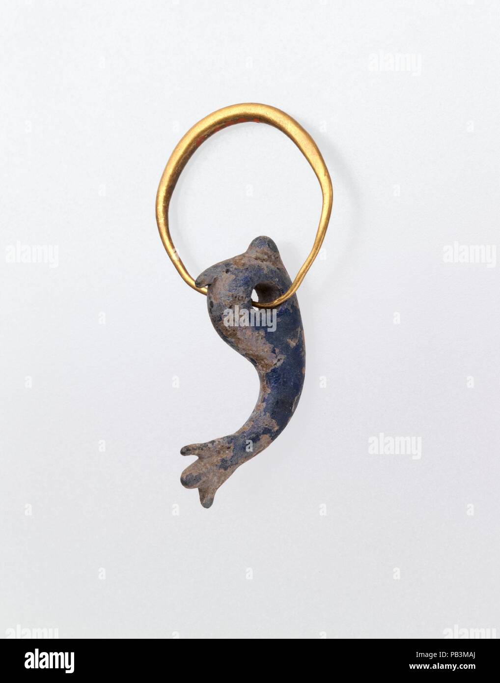 Gold earring with glass pendant in the form of a dolphin. Culture: Roman. Dimensions: Other (Pendant): 11/16 x 3/16 x 1 1/16 in. (1.8 x 0.5 x 2.7 cm)  Diameter (diameter of gold earing): 13/16 in. (2.1 cm). Date: possibly 3rd-5th century A.D..  Glass pendant:  Translucent cobalt blue.  Shaped as a dolphin in the round, with large suspension hole serving as eyes, tooled to form rounded nose, pointed crest, and three-finned tail; small jagged projection under belly.  Intact; dulling, blackish weathering, and iridescence. Museum: Metropolitan Museum of Art, New York, USA. Stock Photo