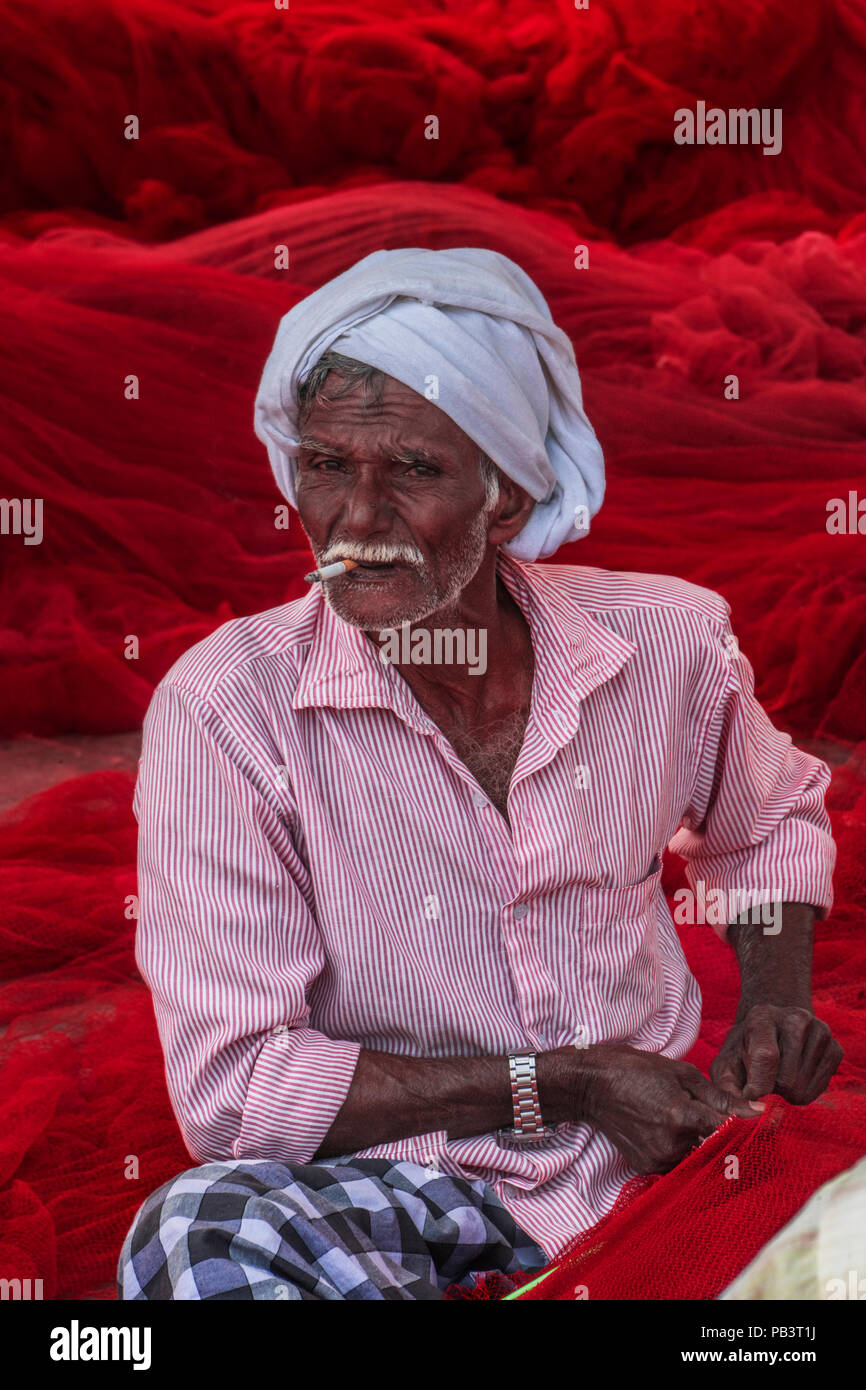 A Keralan fisherman mends one of the local red fishing nets Stock Photo