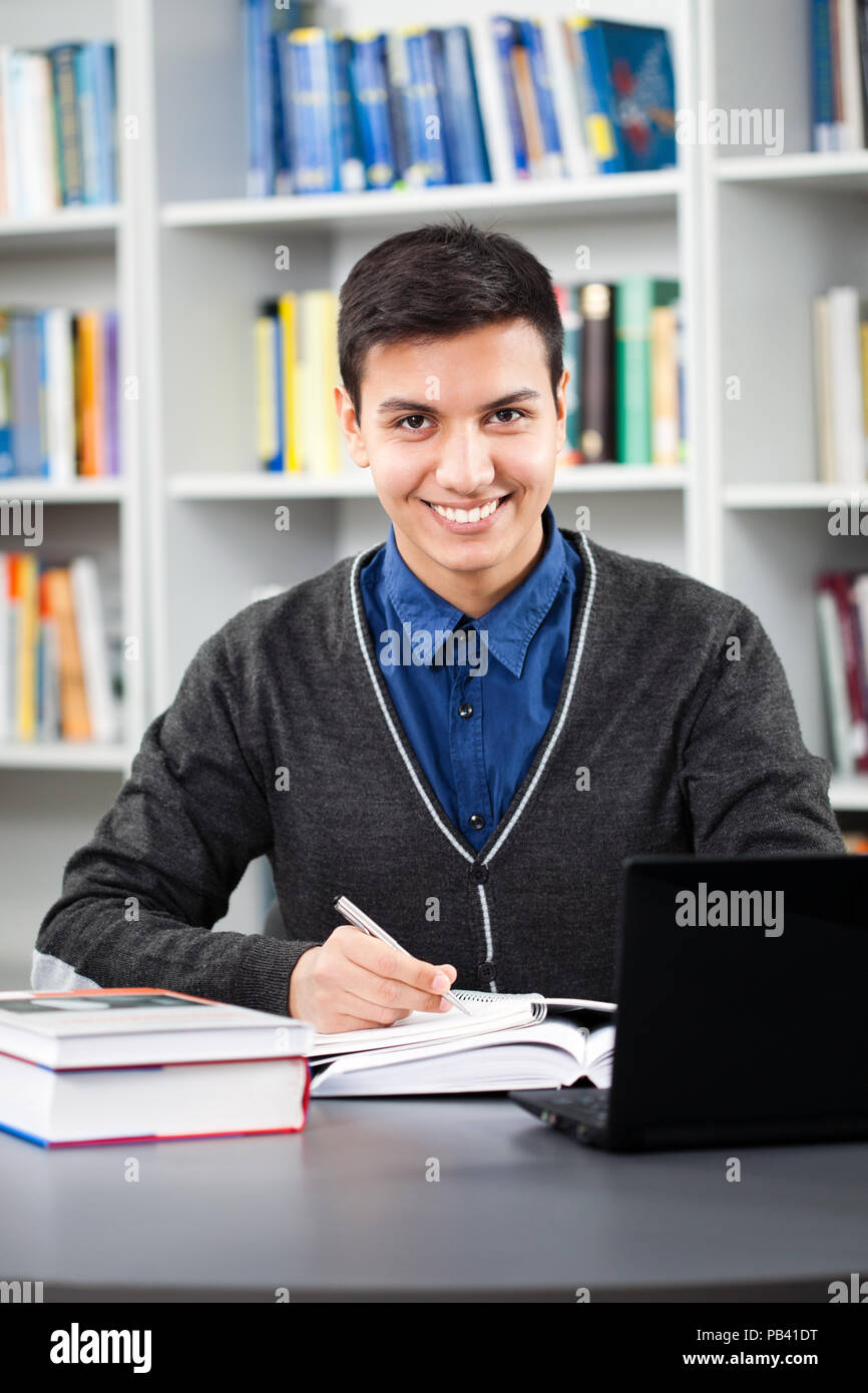 Happy student is learning in library. He is using laptop. Stock Photo