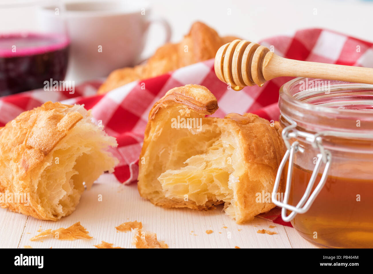 French style breakfast, a white wooden table with glass of fresh beetroot smoothie, croissants and glass bowl of honey, few croissants placed on the r Stock Photo