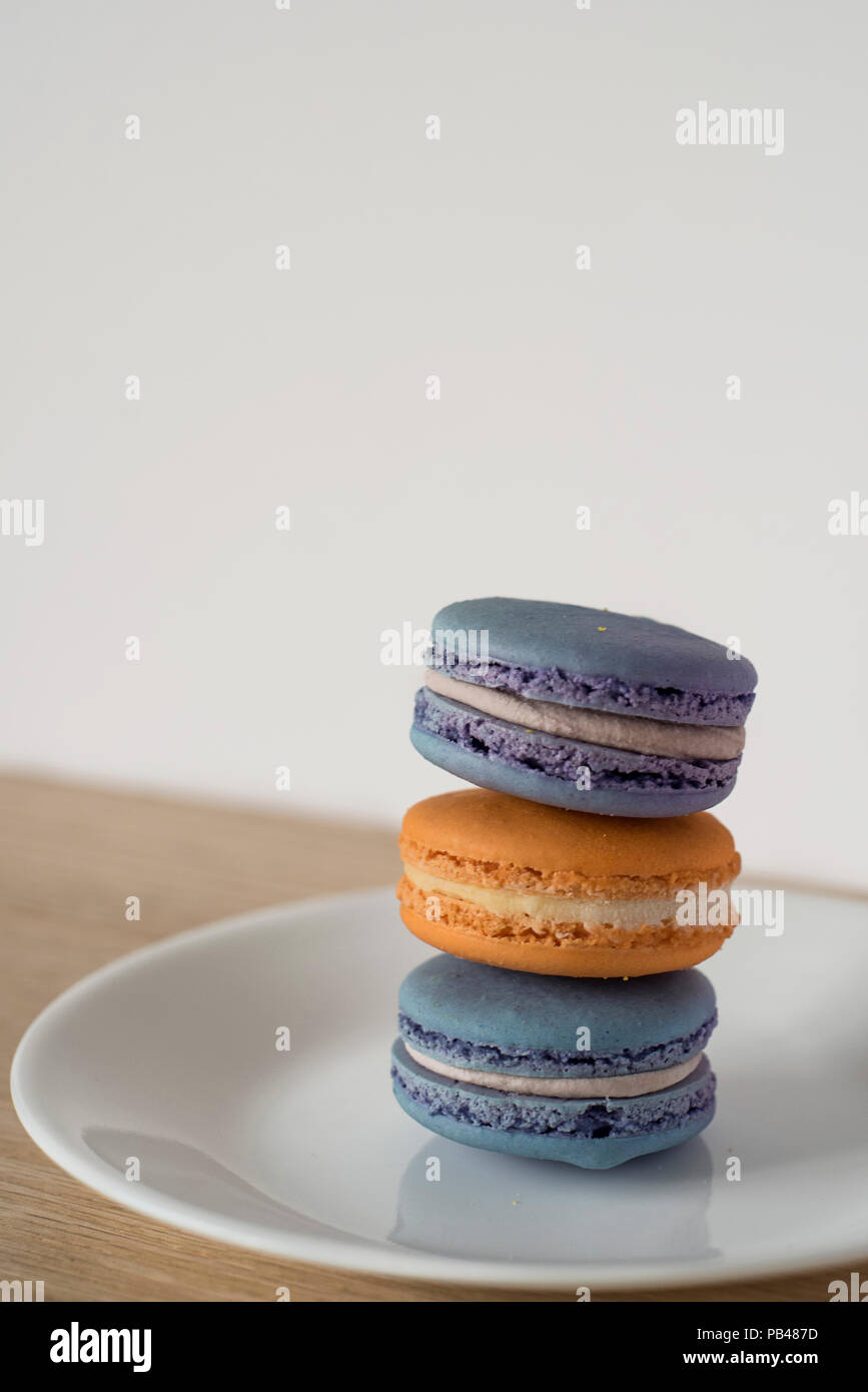 Leaning Macaron Tower in Blue and Orange Sitting on a Plate on a Wooden Counter in Front of a Light Colored Background Ready for Text Stock Photo