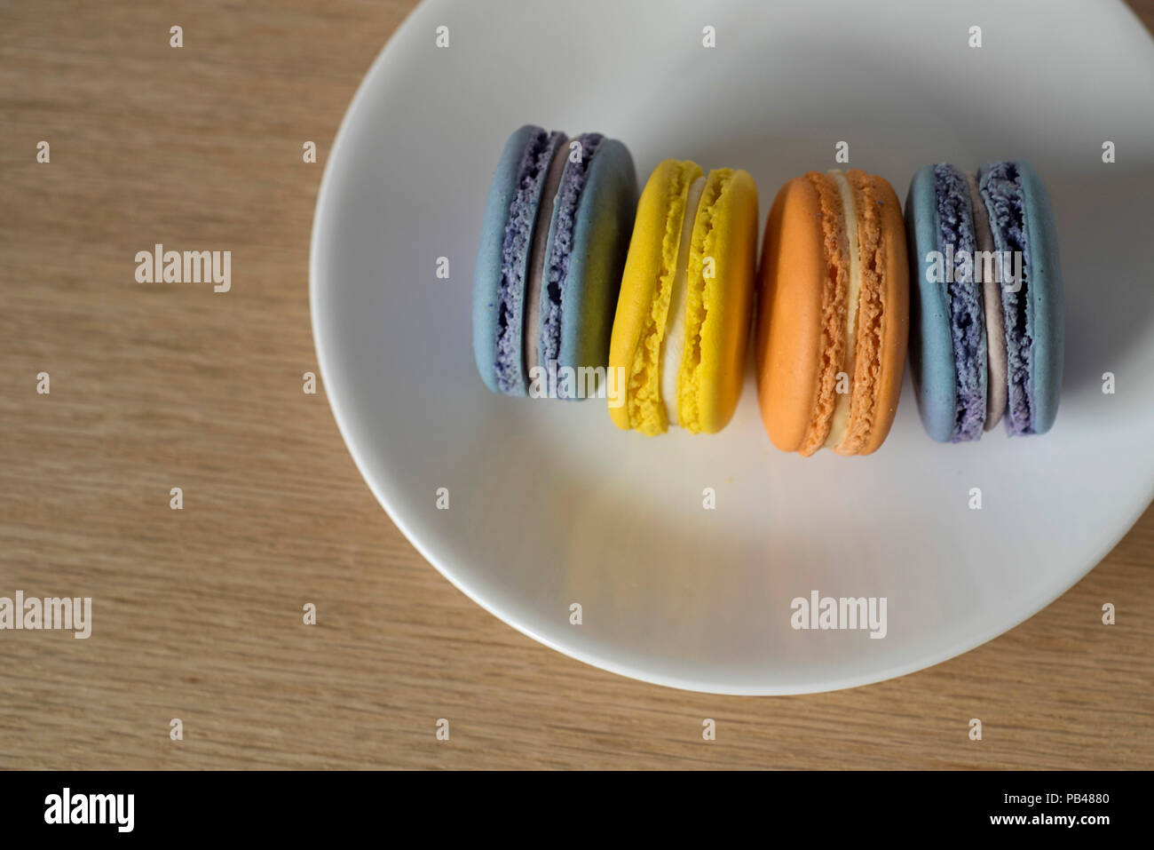 Four Macarons Standing on Their Sides on A White Plate on A Wooden Table Stock Photo