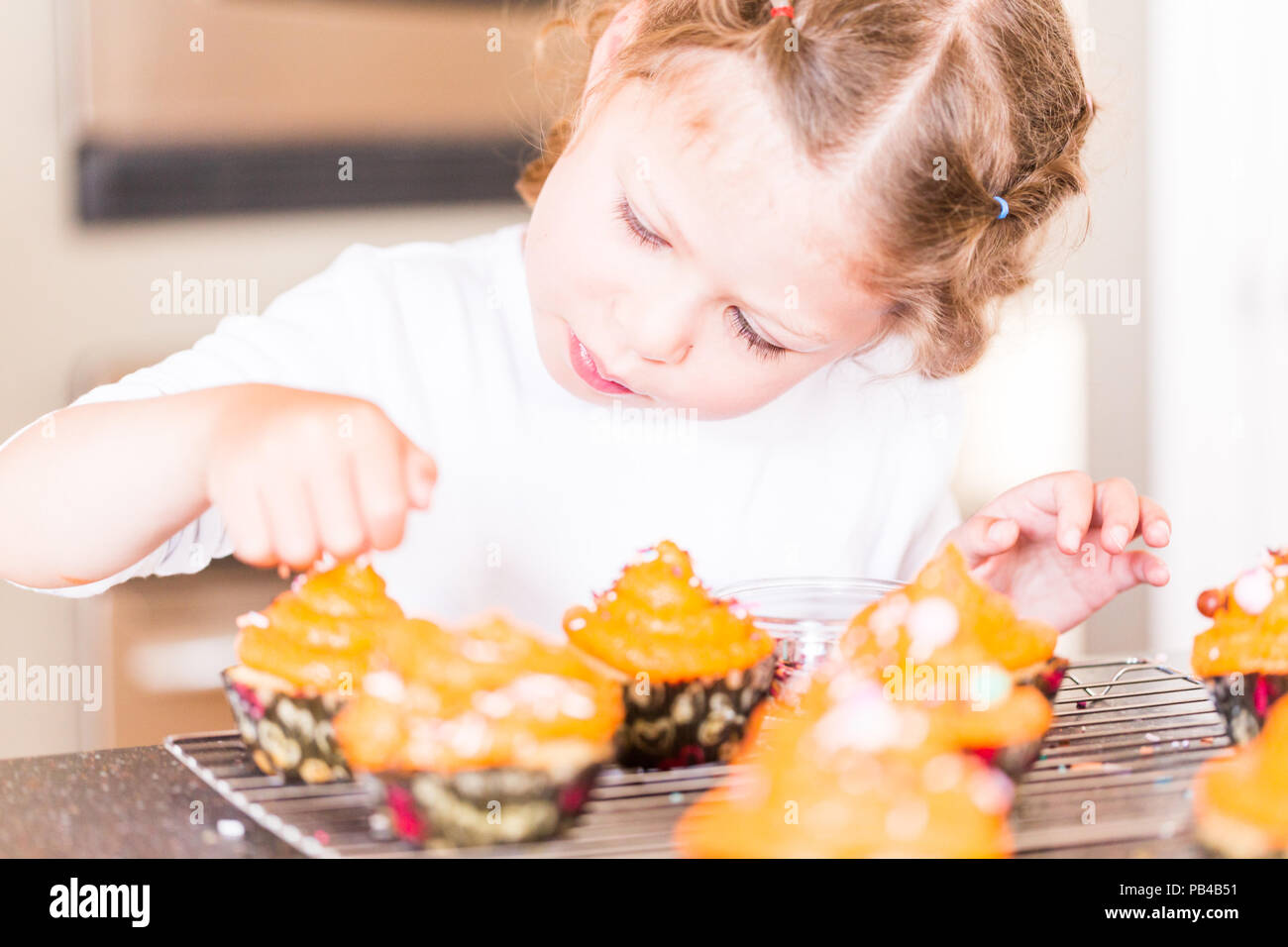 Little girl decorating orange icing on cupcakes with sprinkle mix. Stock Photo