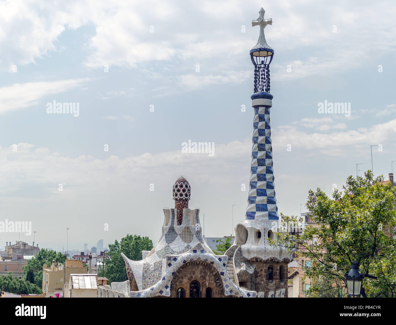 View to the fairytale gingerbread lodge with rooftop terrace crowed with a four-armed cross against the blue cloudy sky in Park Guell, Barcelona, Spai Stock Photo