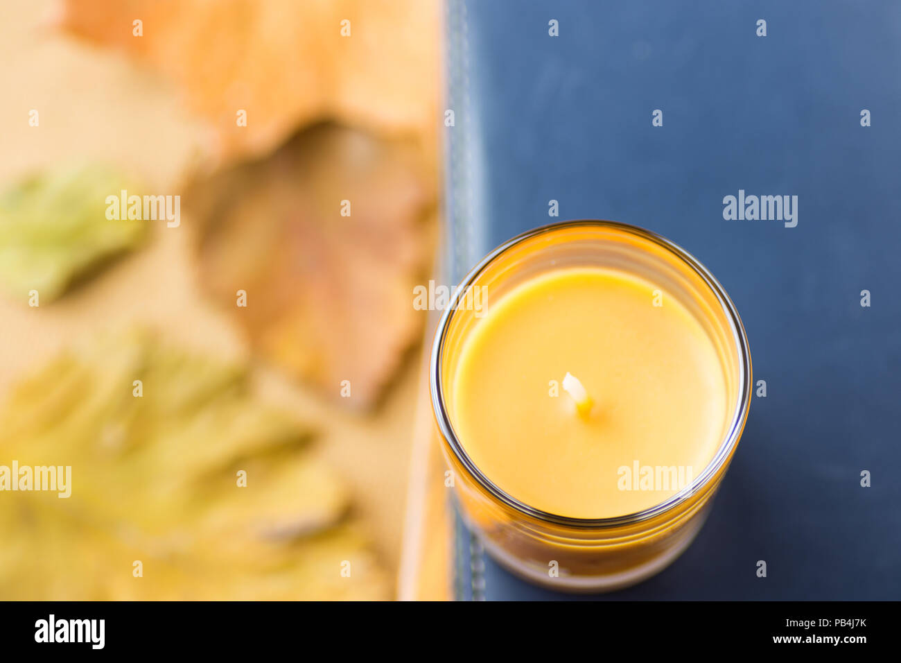 Orange Candle in Glass Holder on Pile of Books Dark Blue Navy Background. Dry Yellow Red Autumn Leaves. Cozy Fall Atmosphere. Poster Banner Template f Stock Photo