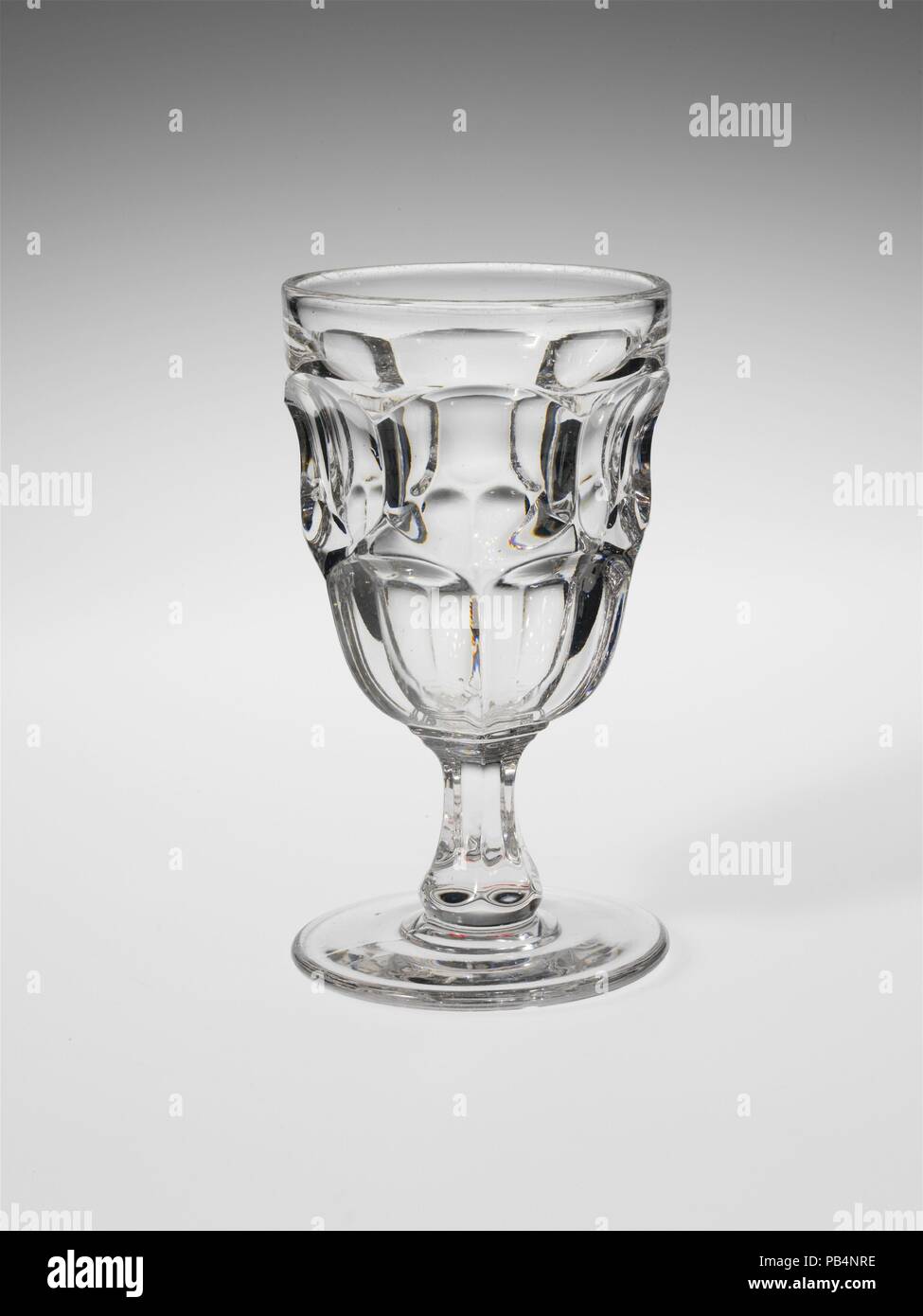 Goblet. Culture: American. Dimensions: H. 6 in. (15.2 cm). Date: 1830-70.  With the development of new formulas and techniques, glass-pressing technology had improved markedly by the late 1840s. By this time, pressed tablewares were being produced in large matching sets and innumerable forms. During the mid-1850s, colorless glass and simple geometric patterns dominated. Catering to the demand for moderately-priced dining wares, the glass industry in the United States expanded widely, and numerous factories supplied less expensive pressed glassware to the growing market. At the Exhibition of th Stock Photo