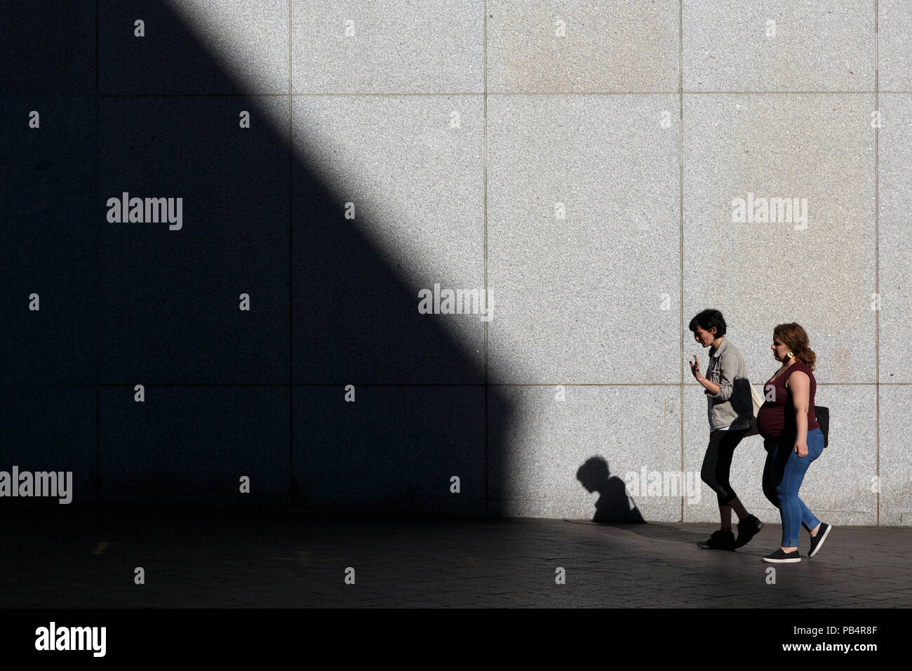 Two people women walking in front of high stone building facade shadow, Boston, Massachusetts Stock Photo