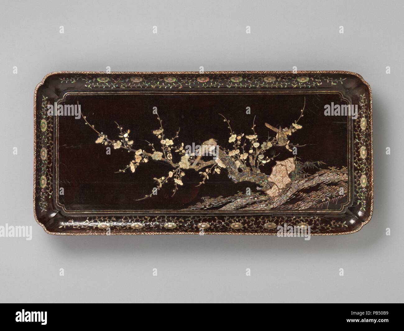 Tray with Flowering Plum and Birds. Culture: China. Dimensions: H. 1 3/4 in. (4.4 cm); W. 11 3/4 in. (29.8 cm); L. 24 3/8 in. (61.9 cm). Date: late 14th century.  The wonderful flowering plum tree and two plump birds that fill the center of this tray illustrate the skillful manipulation of shapes and colors of the inlaid motherof-pearl to create a powerful, dramatic scene. Long narrow pieces of iridescent shell define the rock terrain, while irregular pieces form the clump of rocks in front of the trunk of the flowering plum. Fragments of mother-of-pearl create the craggy trunk of the ancient  Stock Photo
