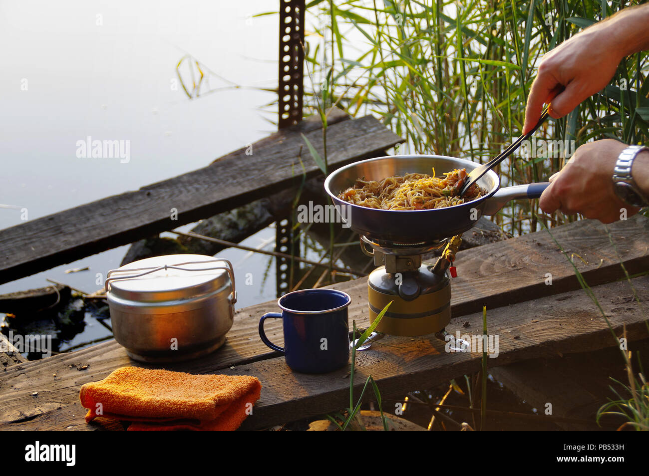 Camping food making. Pasta on pan on tourist fire stove. Camp cooking on the shore of the lake. Stock Photo