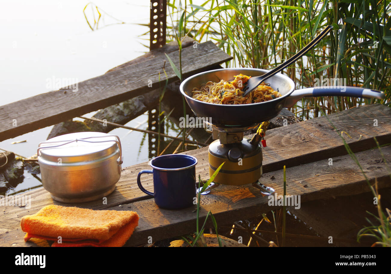 Camping food making. Pasta on pan on tourist fire stove. Camp cooking on the shore of the lake. Stock Photo
