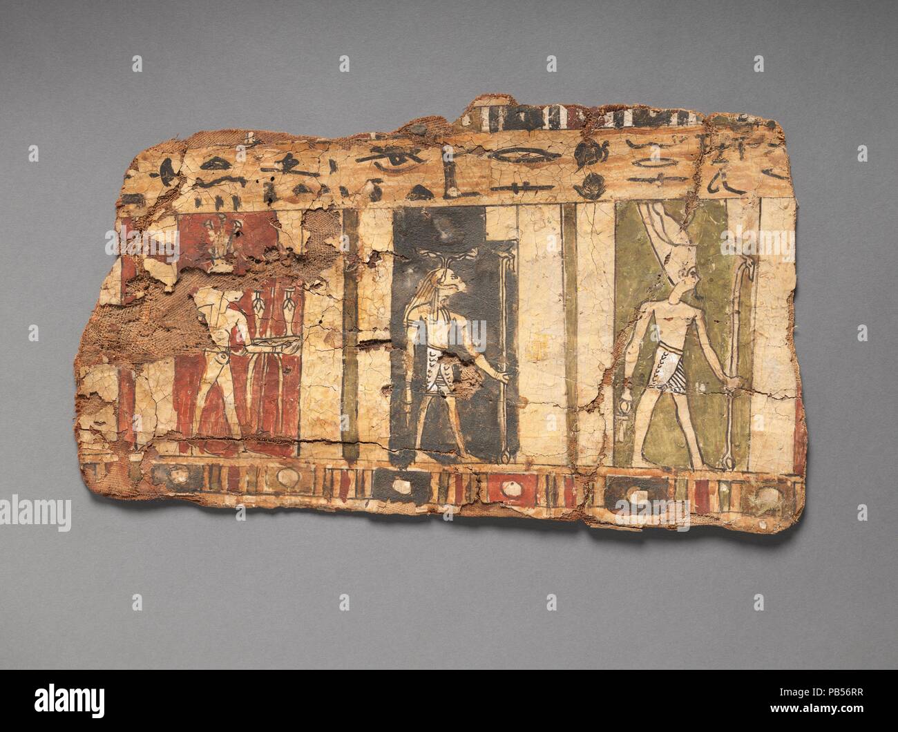 Fragment of cartonnage depicting three deities. Dimensions: H. 20.5 cm (8 1/16 in.); L. 34.4 cm (13 9/16 in.). Date: 200 BC-200 AD.  Designed to encase a mummy, this cartonnage is composed of about seven layers of linen plastered together to form a hard shell. Visible on this fragment are three gods: at the right is the creator god Atum in the double crown; followed by the ram-headed god Khnum; and then Hapy, personification of the fertility brought by the Nile River. An inscription in roughly-sketched hieroglyphs runs from right to left in the band above their heads. The somewhat awkward styl Stock Photo