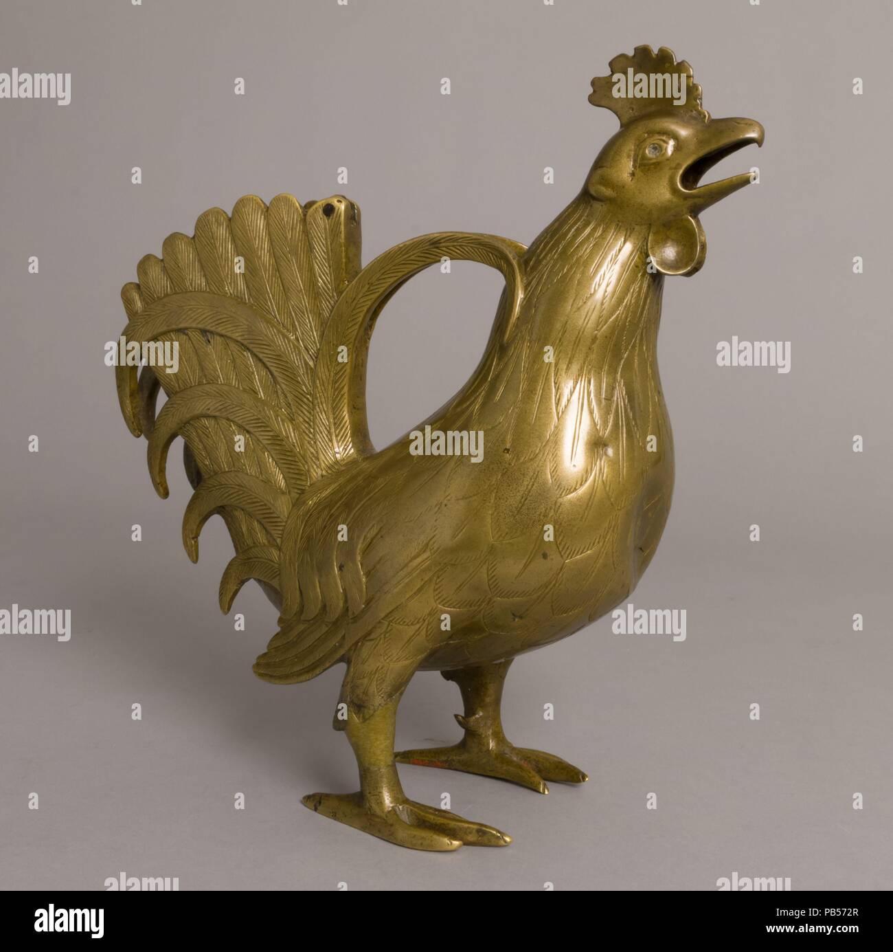 Aquamanile in the Form of a Rooster. Culture: German. Dimensions: 9 15/16 x 4 1/8 x 9 3/4 in. (25.2 x 10.5 x 24.7 cm)  Thickness: 11/16-15/16 in. (0.18-0.24 cm). Date: 13th century.  The rooster's majestic tail feathers splay in rhythmic arcs as he crows, full-throated. The artist who modeled the bird boldly balanced the body on its tiny talons.  This elaborate water vessel was intended for handwashing. A specialty of metalworkers in German-speaking lands for centuries--from the twelfth to the fifteenth--they are called aquamanilia, from the Latin words for water (aqua) and hand (manus). Museu Stock Photo