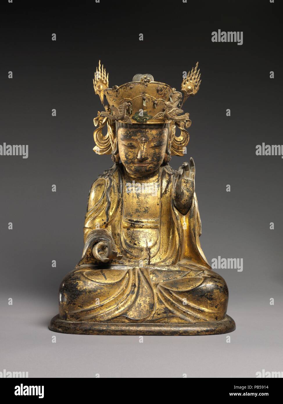 Seated bodhisattva (left attendant of a triad). Culture: Korea. Dimensions: H. 20 1/4 In. (51.4 cm); W. 14 1/4 in. (51.4 cm); D. 12 3/4 in. (36.2 cm)  H. to flame elements: 21 1/2 in. (54.6 cm). Date: ca. mid- 17th century.  This elegant figure represents a bodhisattva--a compassionate, enlightened being who has chosen to remain on earth to help mortals attain enlightenment. This statue was originally one of two attendant bodhisattvas that flanked a Shakyamuni or Amitabha Buddha. The tall, ornate crown, oblong face, and drapery with cascading folds indicate that the statue was likely produced  Stock Photo