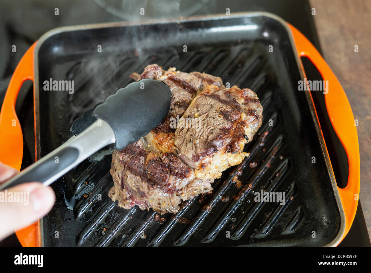 Cooking meat on cast iron grill pan indoors at home. Person turning ribeye  steak on other side with tongs Stock Photo - Alamy