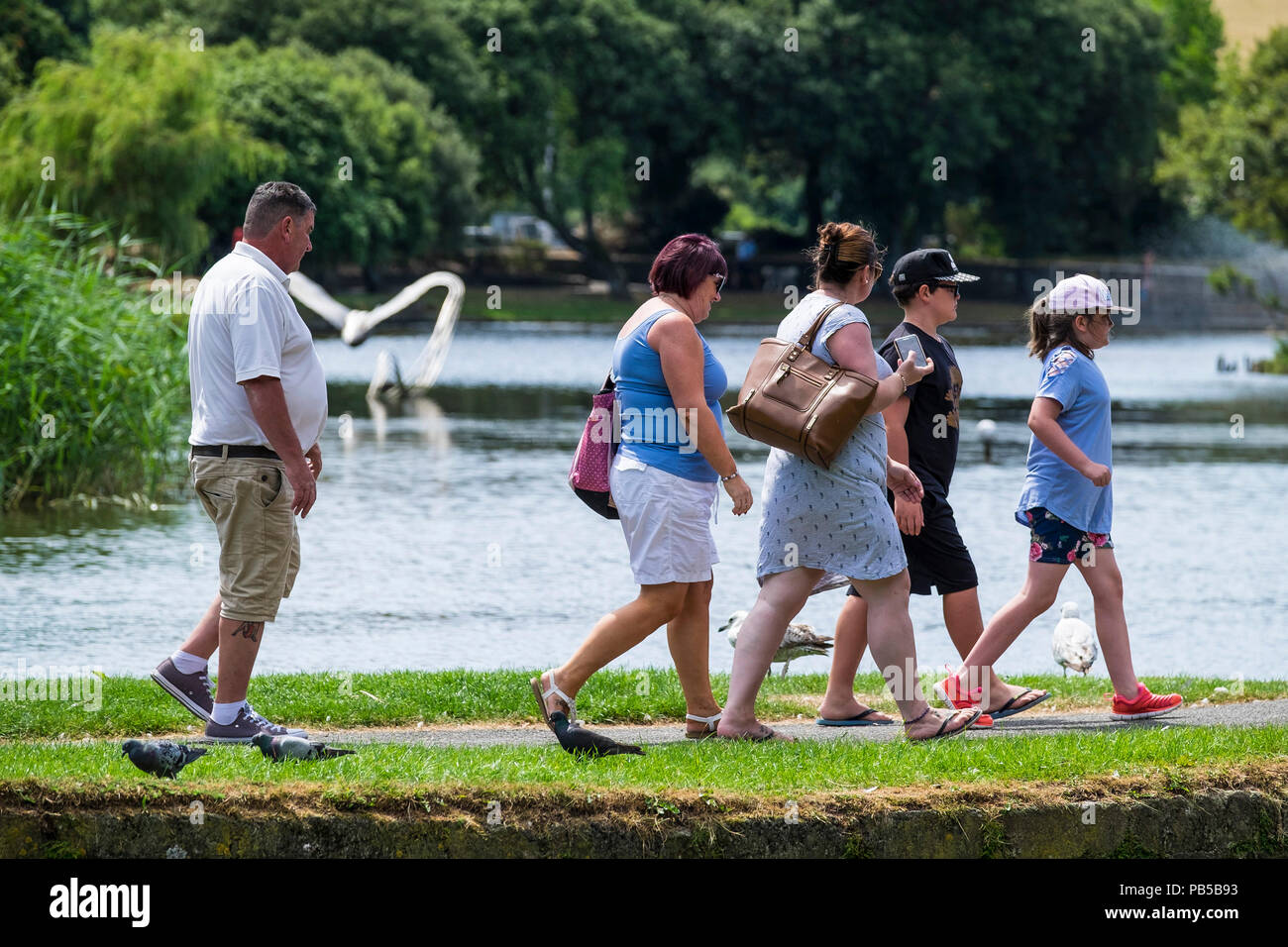 A family of British holidaymakers walking along the bank of a lake in Trenance Garden in Newquay Cornwall. Stock Photo