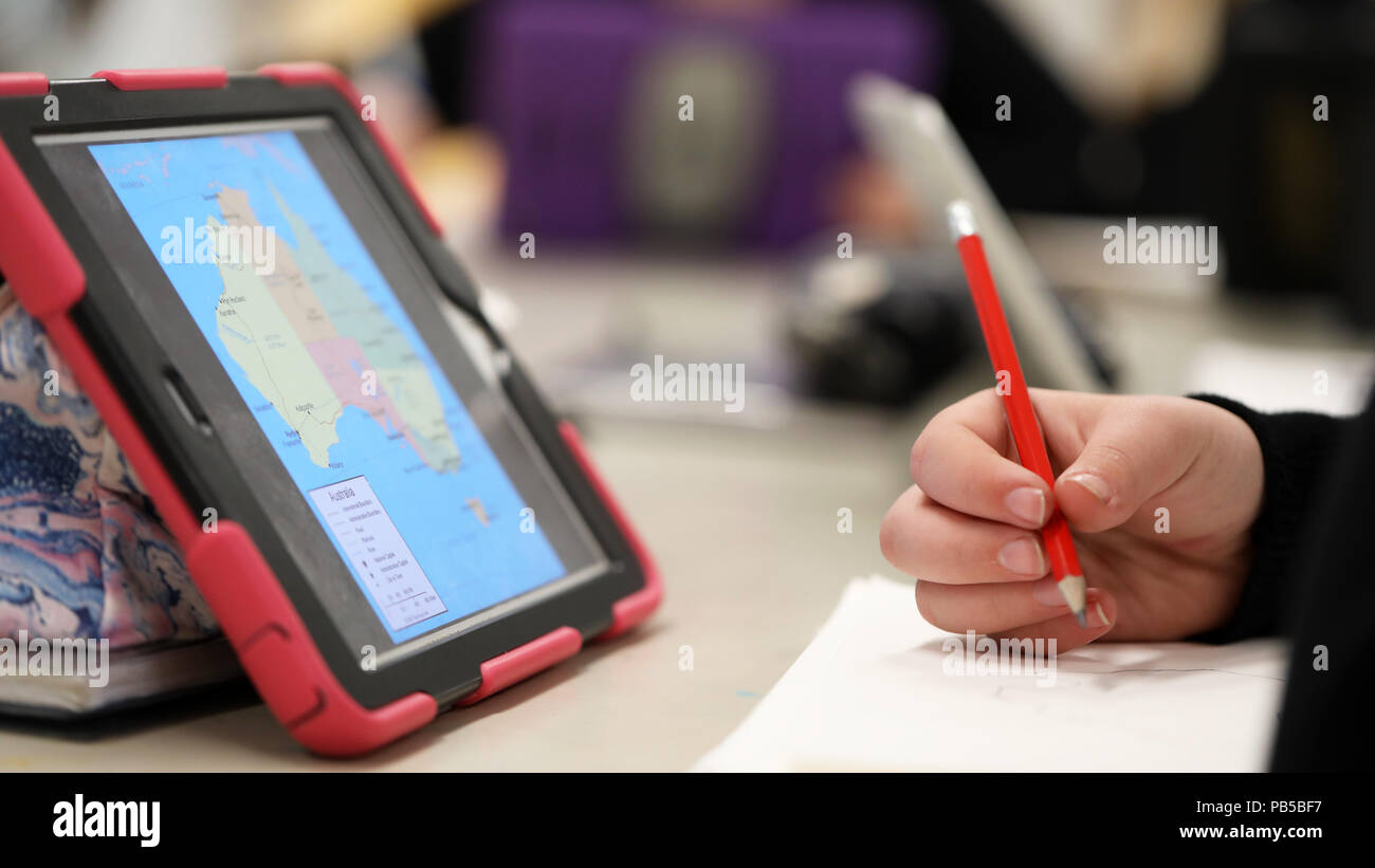 school student with a pencil in their hand with an ipad electronic device or tablet researching. map of Australia on the touch screen. geography atlas Stock Photo