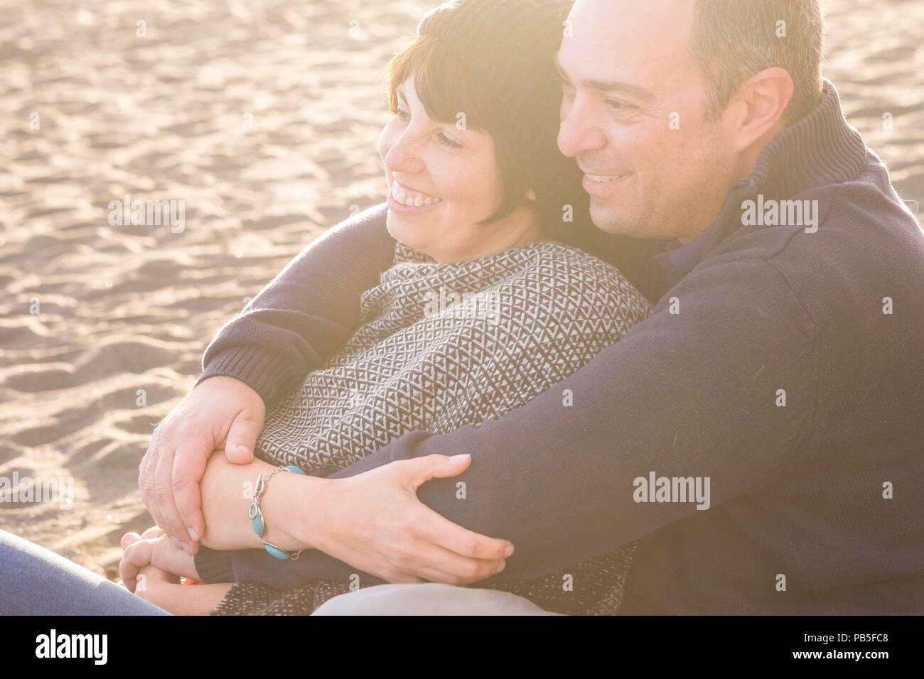 nice beautiful middle age 40 years old couple man and woman caucasian hugged and stay together on the beach sitting in the sand and enjoying a golde a Stock Photo