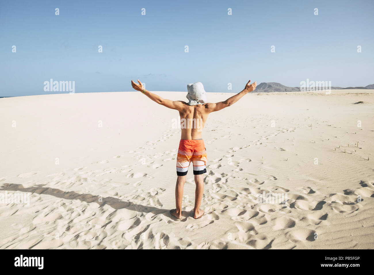young teenager caucasian male enjoy the freedom and the holiday vacation standing with open arms at the beach in the desert dunes. mountain in backgro Stock Photo