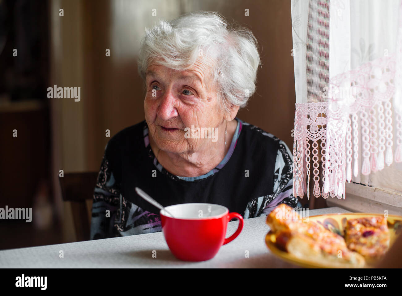 Old lady is sitting at the kitchen table. Stock Photo