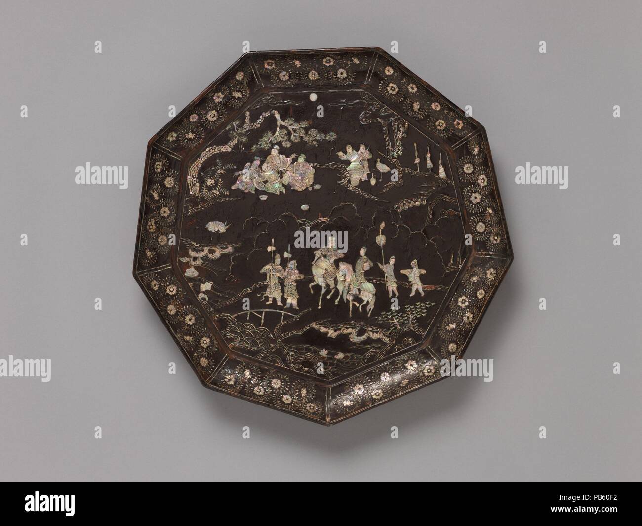 Tray with Figures in a Landscape. Culture: China. Dimensions: H. 2 1/8 in. (5.4 cm); Diam. 19 1/4 in. (48.9 cm); Diam. of foot 17 in. (43.2 cm). Date: 14th century.  The two gentlemen on horseback and their attendants are presumably traveling to join the four figures drinking beneath the pine tree at top. The crane standing near the attendants serving wine and the deer resting at right are symbols of immortality. They add an otherworldly element to the scene, which represents either a paradisiacal realm or the retirement villa of a senior official equipped with the trappings of such a magical  Stock Photo