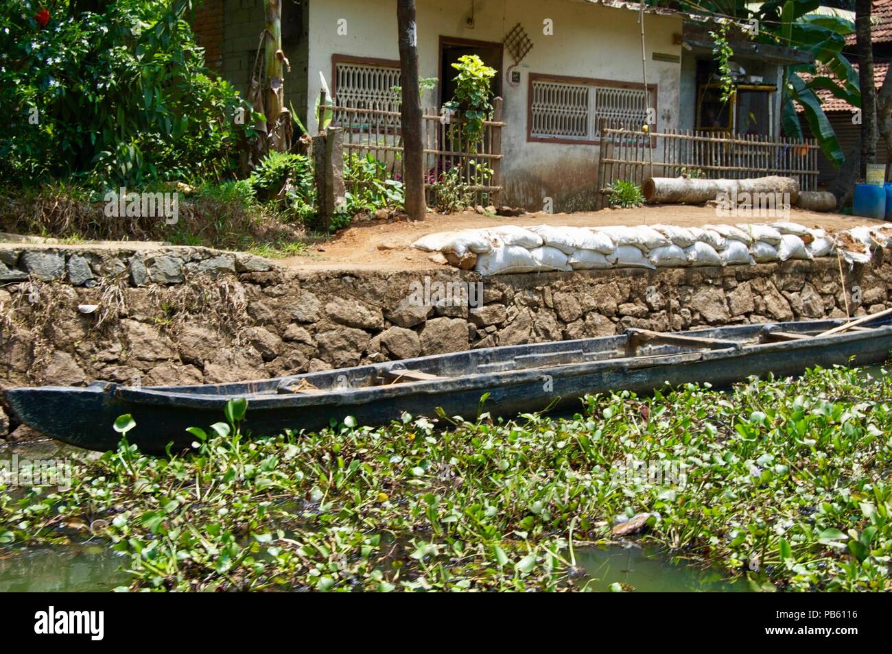 Scenic landscape in rural Kerala (India) close to Kochi: House with stone wall, lush greenery and a wooden boat in the backwaters Stock Photo