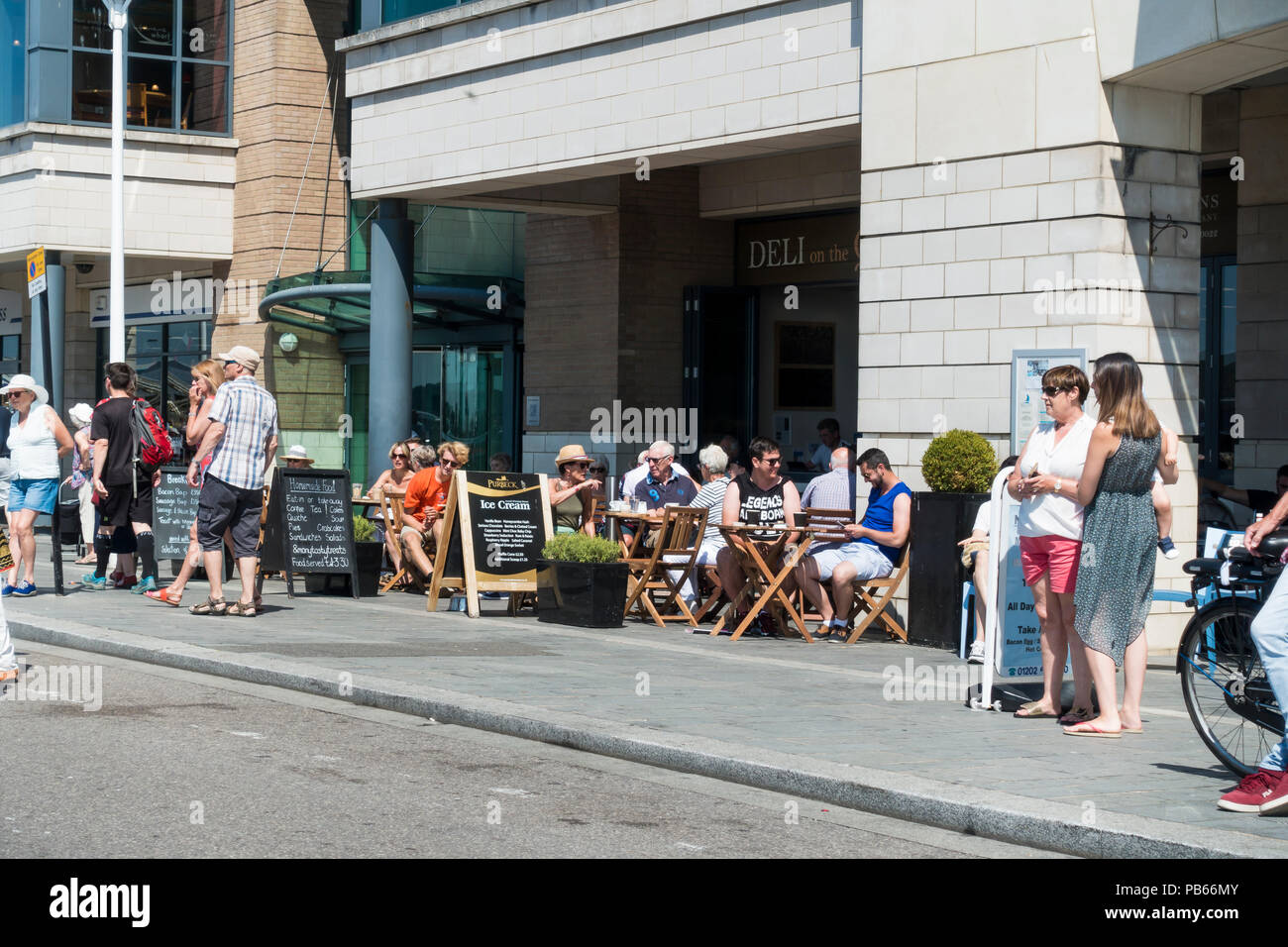 People enjoying a lovely sunny morning, sitting outside a cafe on Poole Quay in the summer season, Poole, Dorset, United Kingdom Stock Photo