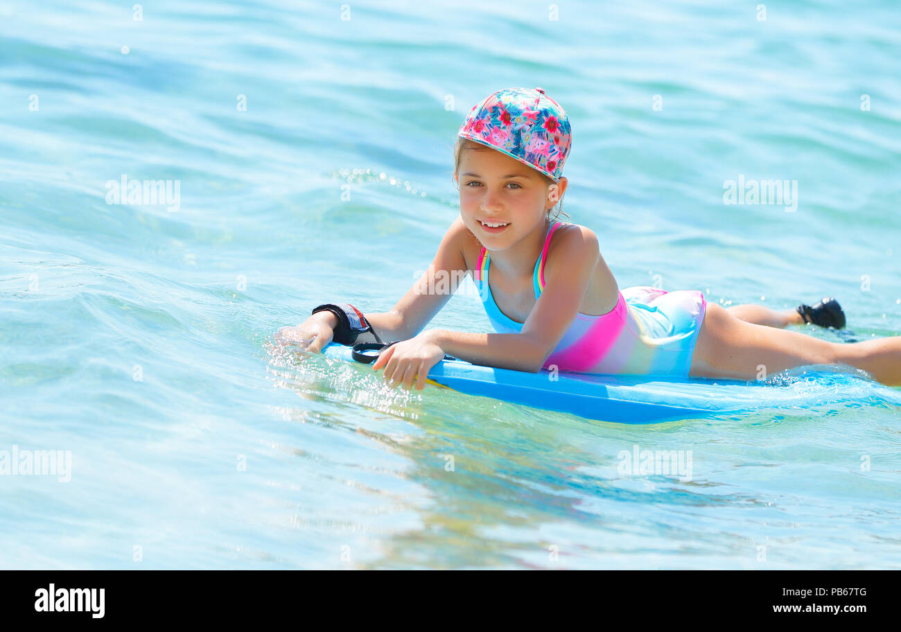 Happy little girl with bodyboard in blue transparent sea, enjoying