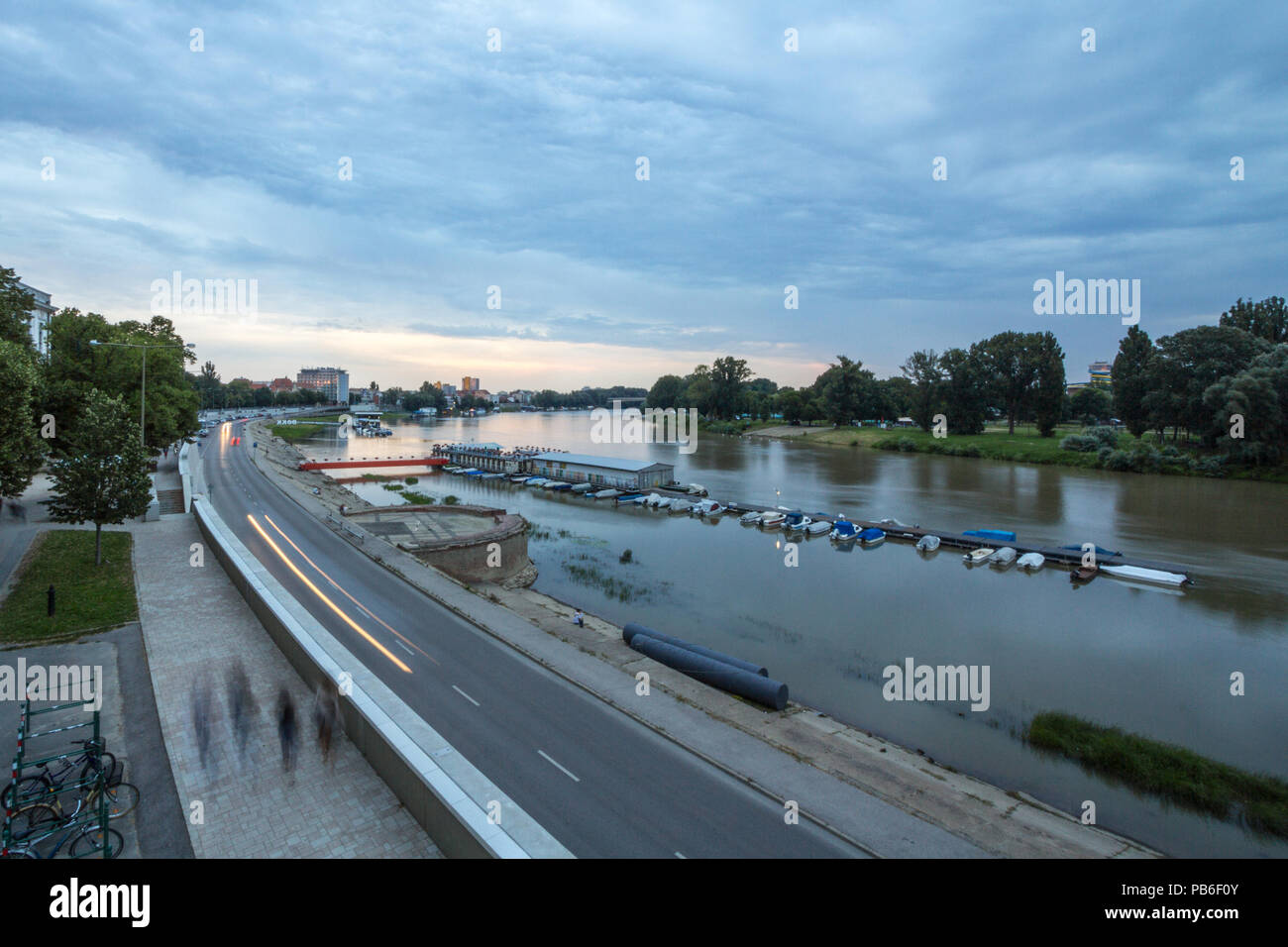 SZEGED, HUNGARY - JULY 4, 2018: Tisza river banks in Szeged city center, seen into the light during sunset during a cloudy summer afternoon. Szeged is Stock Photo