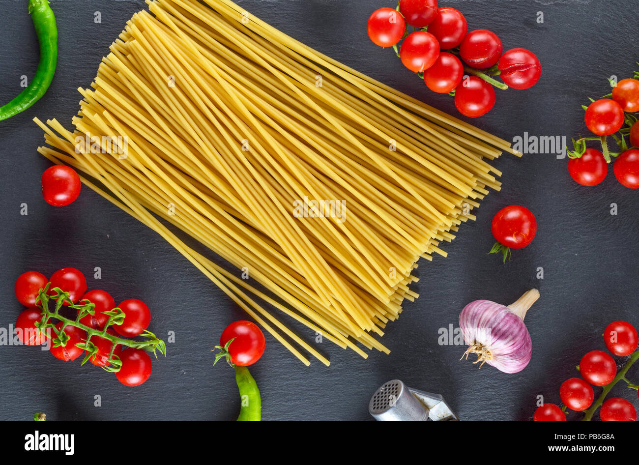 Uncooked pasta spaghetti on black background, red cherry tomatoes and garlic for sauce, top view Stock Photo