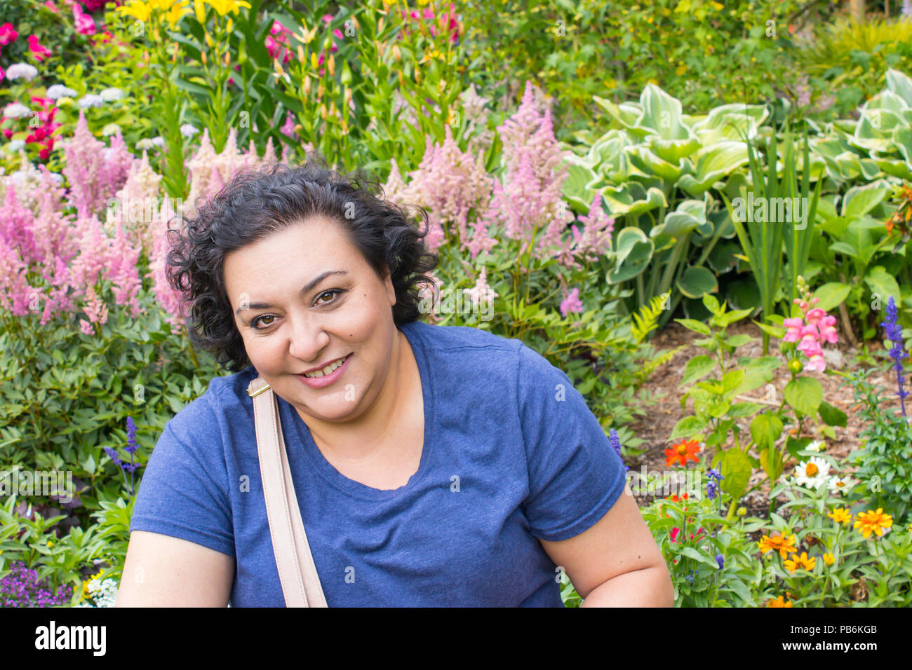 head and shoulders shot of a woman standing in front of pink flowers in a garden Stock Photo