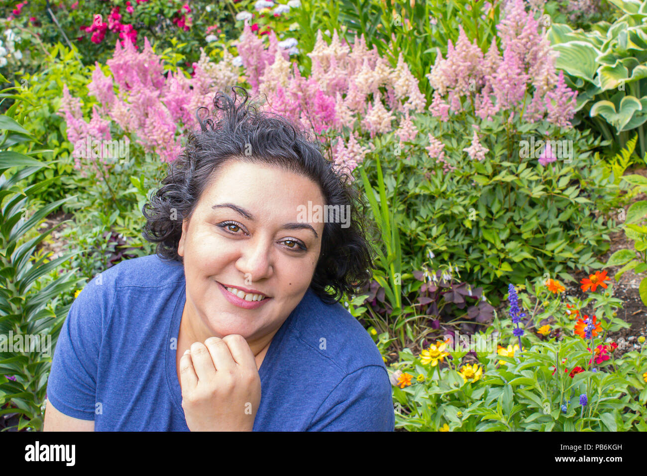 head and shoulders shot of a woman standing in front of pink flowers in a garden Stock Photo